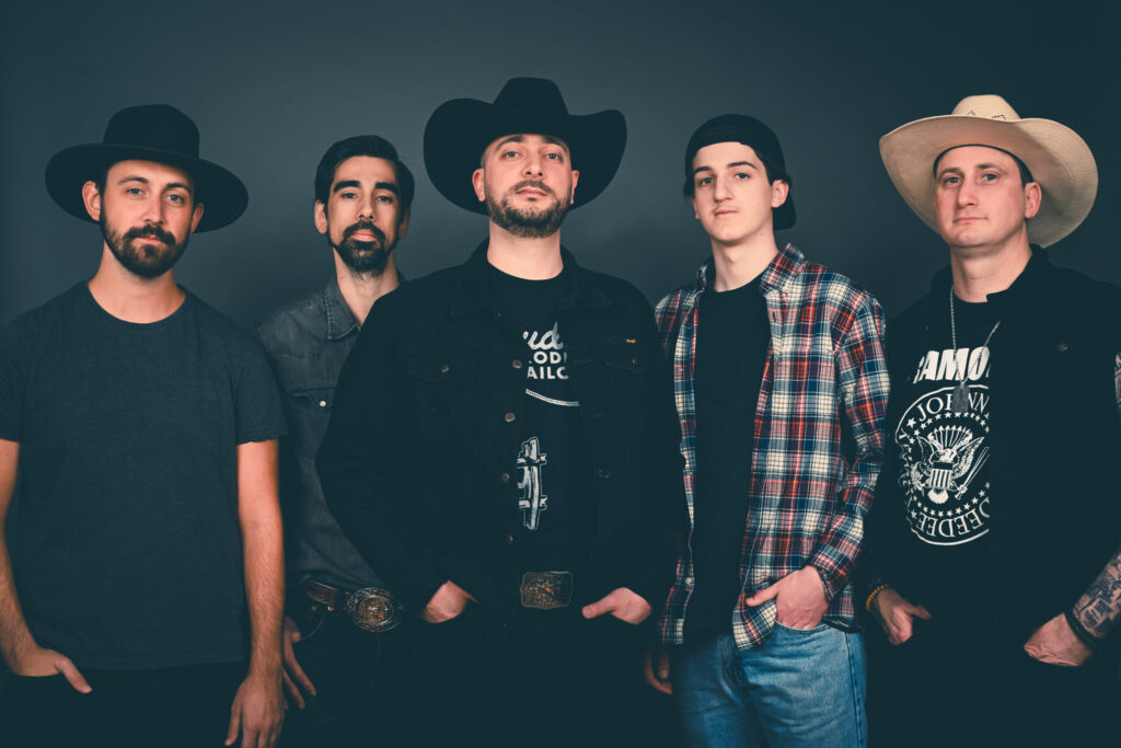 Group portrait of five men wearing cowboy hats standing against a dark backdrop.